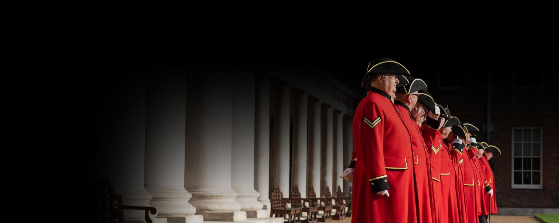Chelsea Pensioners in their scarlet uniforms standing in a line at Royal Hospital Chelsea as part of Remembrance