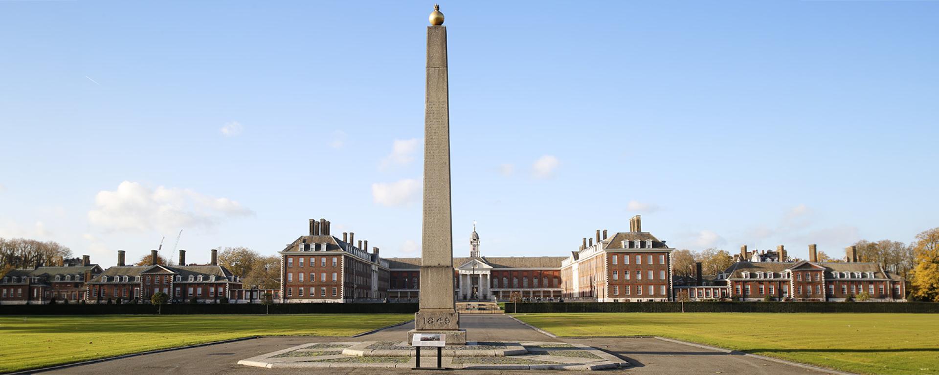 Chilianwala Obelisk Memorial situated in the grounds of the Royal Hospital Chelsea, set against a blue clear sky with the Royal Hospital buildings in the background.