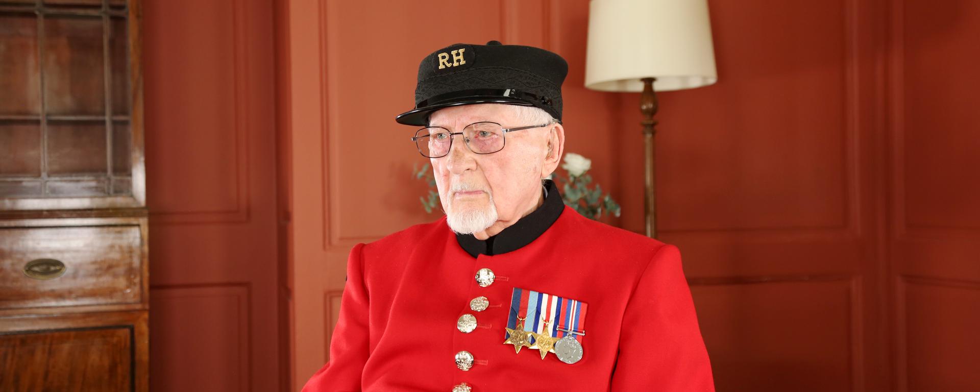 Chelsea Pensioner Brian sitting on a chair in his red scarlet uniform