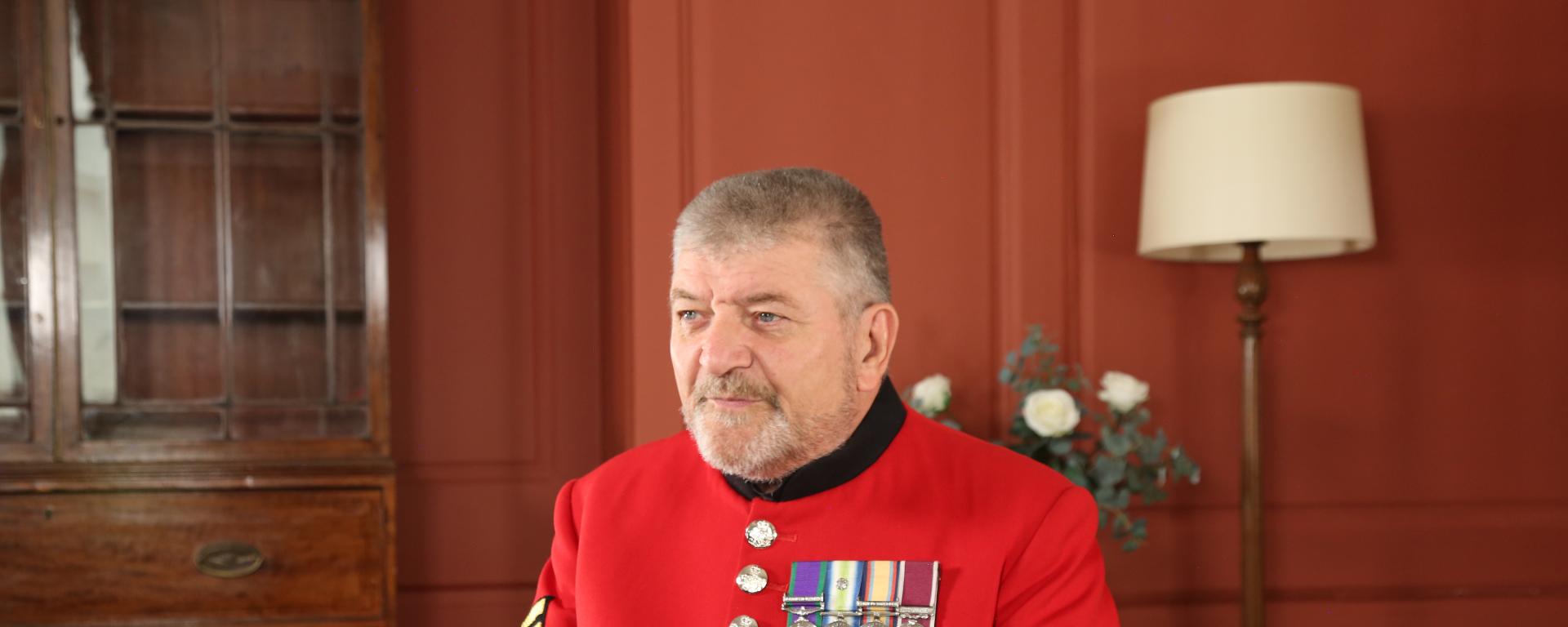 Chelsea Pensioner Paul Sinclair sitting on a chair in his red scarlet uniform