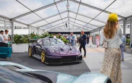 A purple sports car with yellow wheels is positioned in a luxurious outdoor marquee, with multiple people spectating besides the car