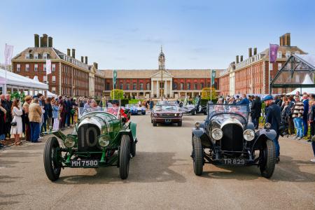 Vintage racing cars lined up in the central courtyard of the Royal Hospital Chelsea, with crowds gathered on either side and the historic red-brick buildings in the background.