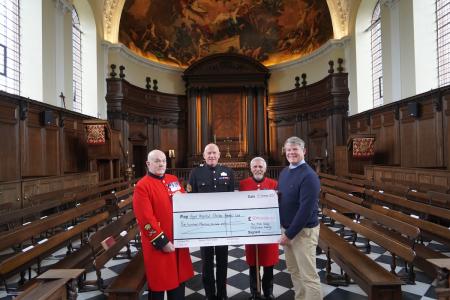 Two Chelsea Pensioners, dressed in their iconic scarlet uniform, are presented a large high value check by 2 donors in the opulent wood panelled Wren Chapel.