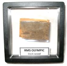 A framed wooden fragment labelled “RMS Olympic – Deck wood.” The object is mounted within a display case, presented as a preserved piece of the historic ocean liner.