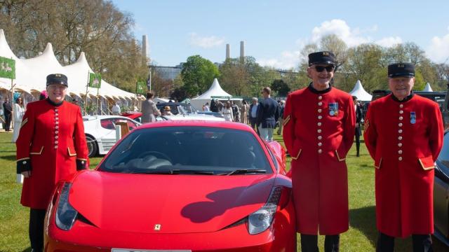 Chelsea Pensioners stand alongside a red Ferrari during the Salon Privé luxury car show