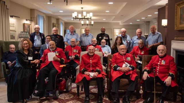 Group of Chelsea Pensioners in scarlet and blue uniforms sitting in a group with guests from Korean community