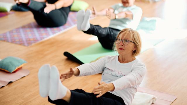 A group of senior women engaged in various yoga and pilates exercised on colourful mats on a wooden floor.