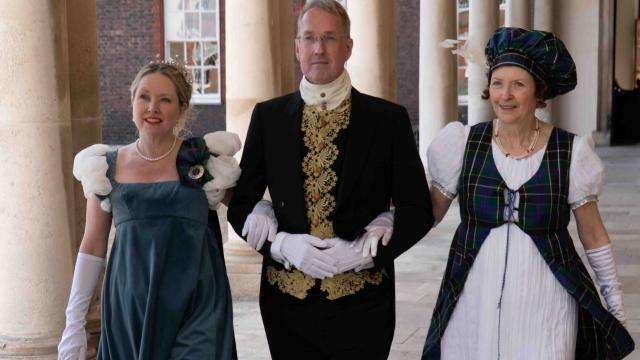 A man and two women stand beneath a colonnade in period costume reflecting the Waterloo Era
