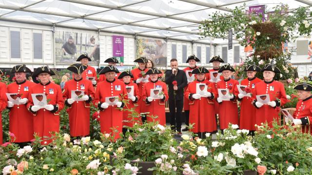 A group of Chelsea Pensioner Signgers stand with music books amongst flowers at the Chelsea Flower Show.