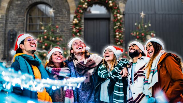 a group of friends dressed in Christmas hats and winter coats are laughing together in front of a festive decorated Soane Stable Courtyard