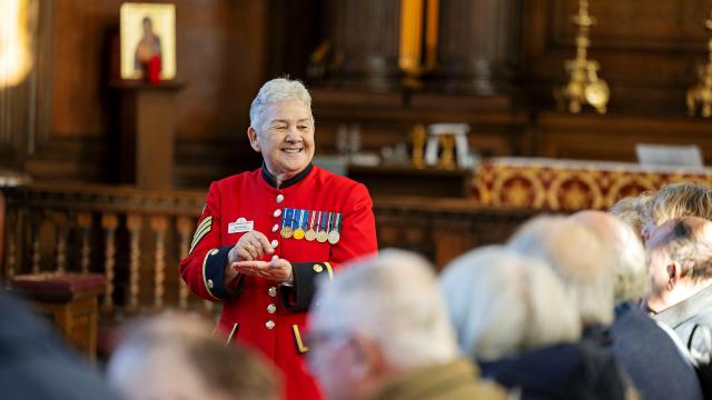 Chelsea Pensioner in a scarlet uniform with medals addressing a seated audience inside the chapel at the Royal Hospital Chelsea.