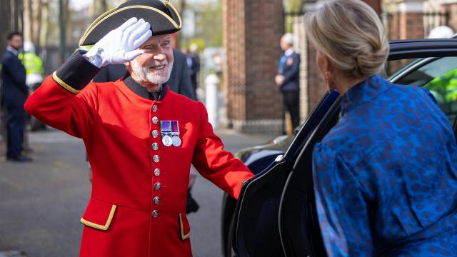 A Chelsea Pensioner in scarlet uniform saluting as the Duchess of Edinburgh arrives beside a car at the Royal Hospital Chelsea.