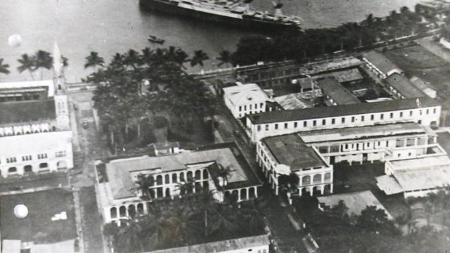 A vintage black and white aerial shot showing a small harbour town with a large ship moored at its dock