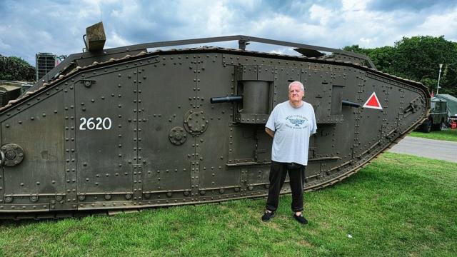 An image of a man standing in front of a tank in a green space, promoting the Hands-On History: World War One Artifacts event at Royal Hospital Chelsea.