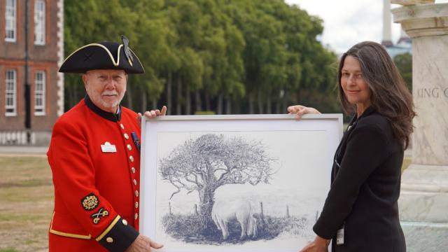 An image of Chelsea Pensioner Roy Palmer holding up a painting alongside a woman at Royal Hospital Chelsea