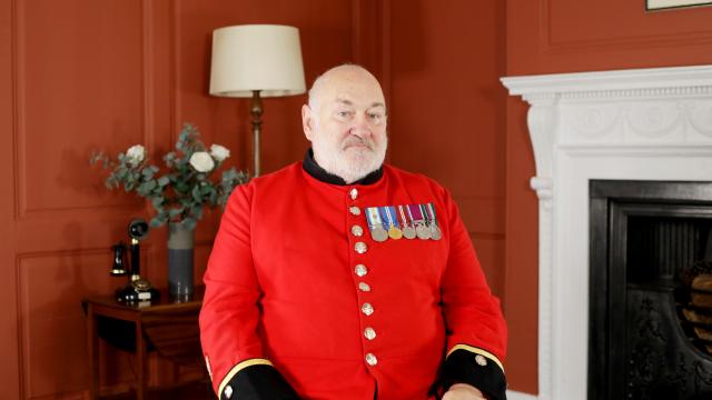 Chelsea Pensioner David Pratt sitting on a chair in his red scarlet uniform